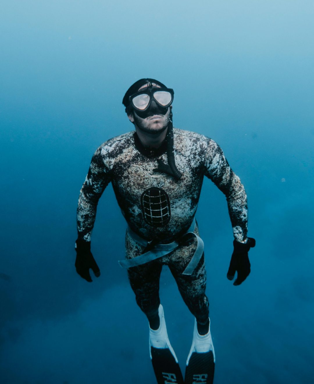 Freediver in camouflage suit exploring the depths of Hilo, Hawaii underwater.