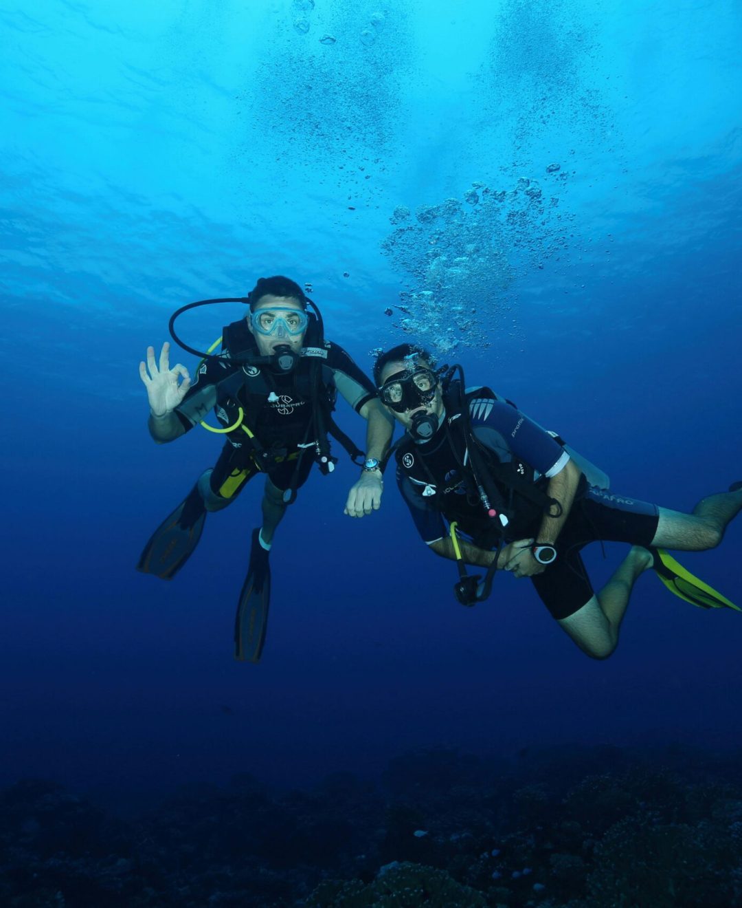 Two scuba divers with gear exploring the deep blue ocean, captured under natural light.