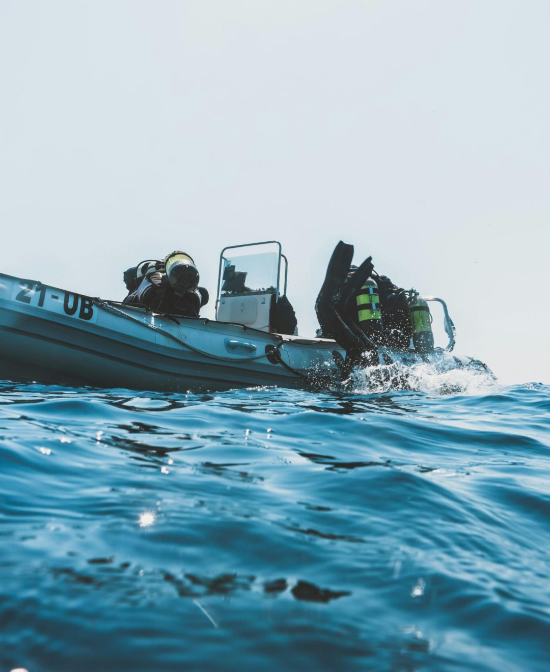 Scuba divers equipped for an ocean dive prepare from an inflatable boat on a sunny day.