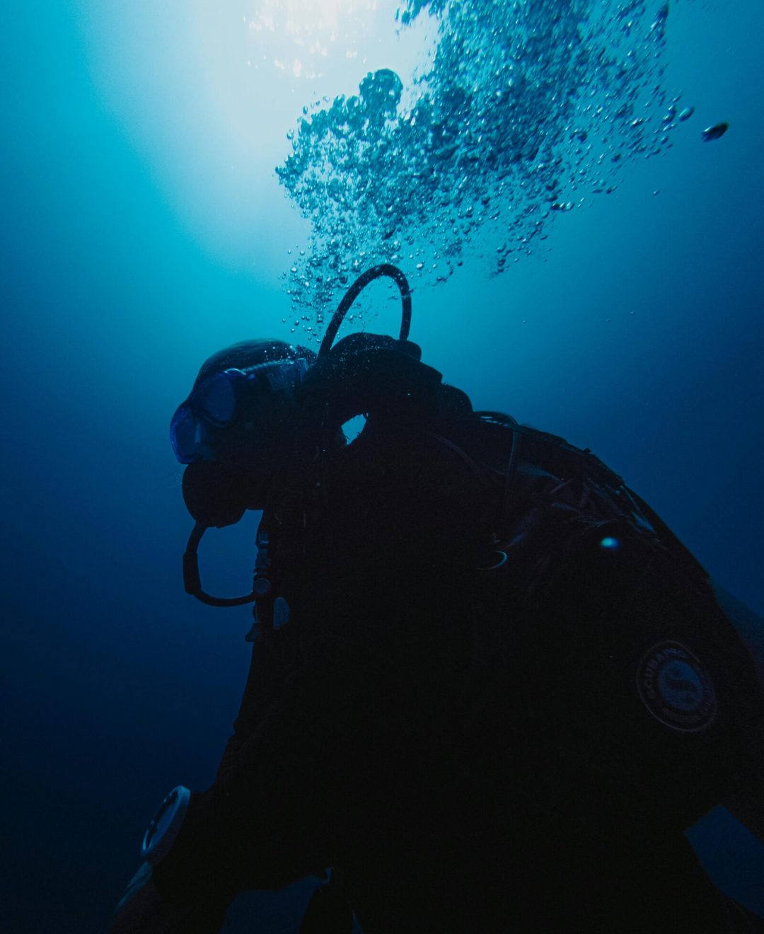 Scuba diver exploring the deep blue ocean beneath sunlight, bubbles rising.
